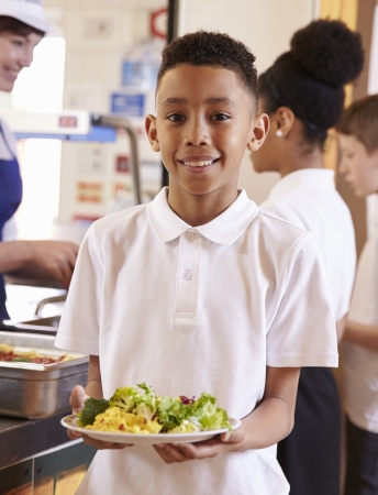 Kid in line holding a plate of food and smiling