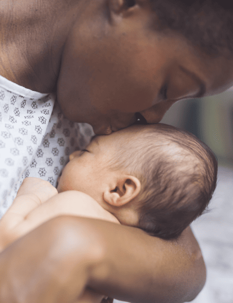 Black woman in hospital gown kissing head of newborn baby